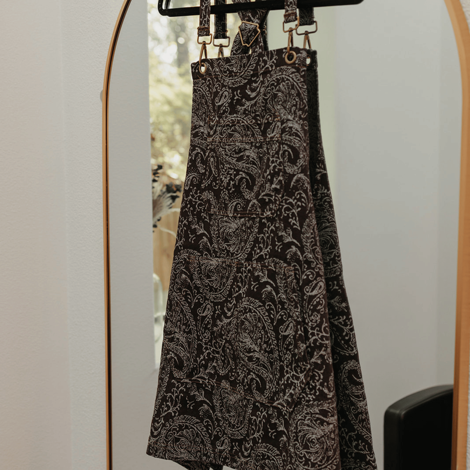 The Outlaw apron by J Clark Designed displayed on a hanger that is hung over a mirror