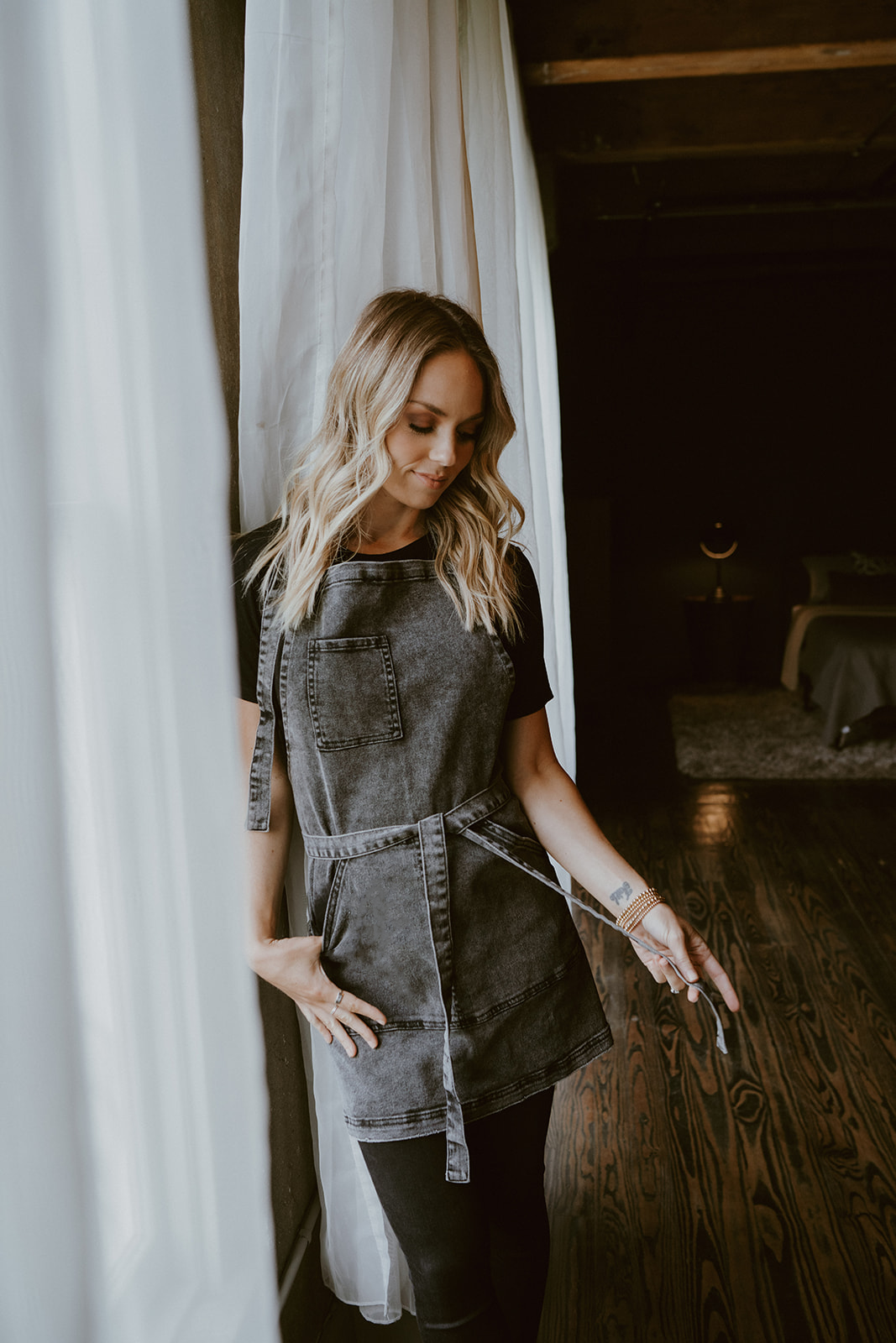 Black acid washed denim apron by J Clark Designed worn by female model playing with waist ties.