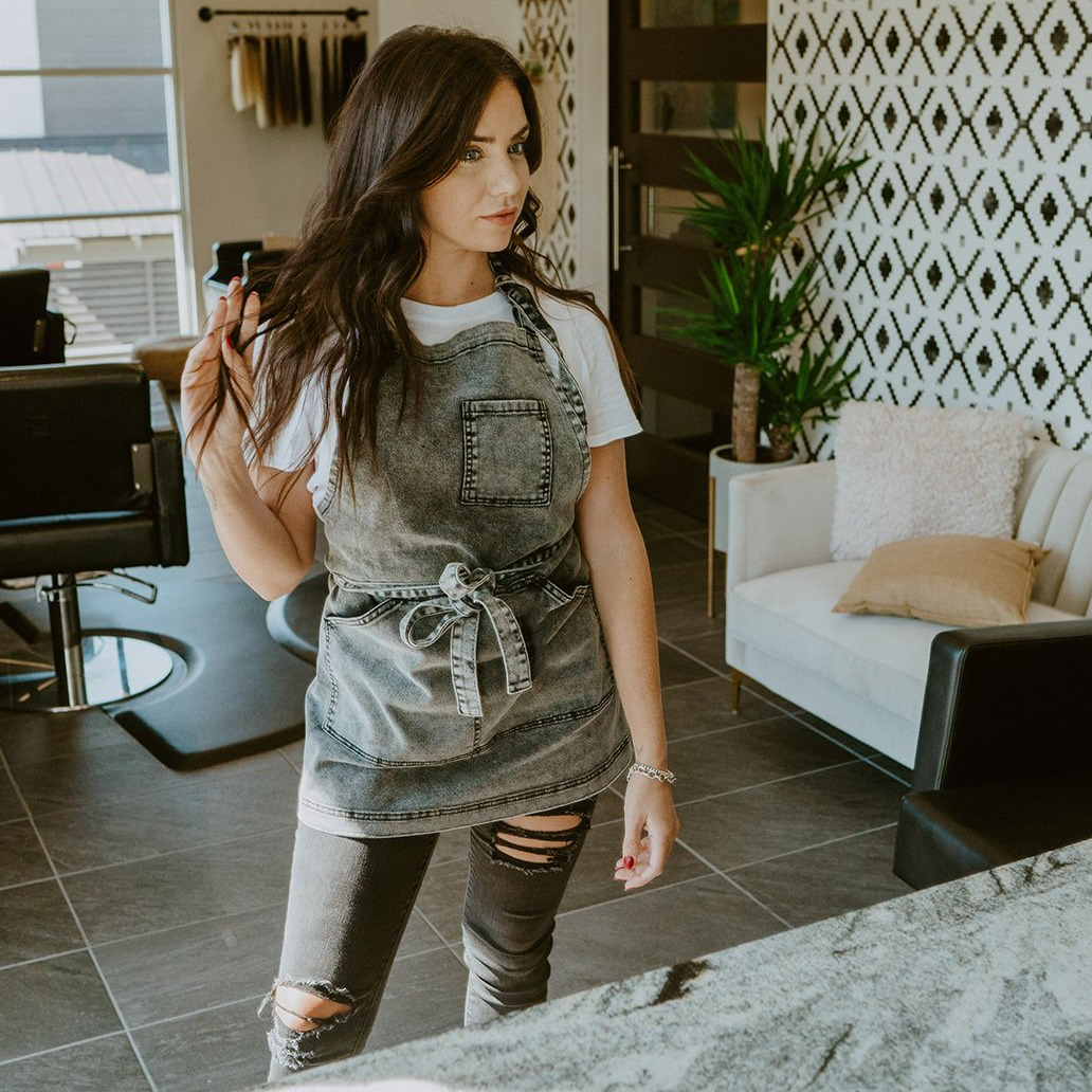 Black acid washed denim apron by J Clark Designed worn by woman playing with her hair