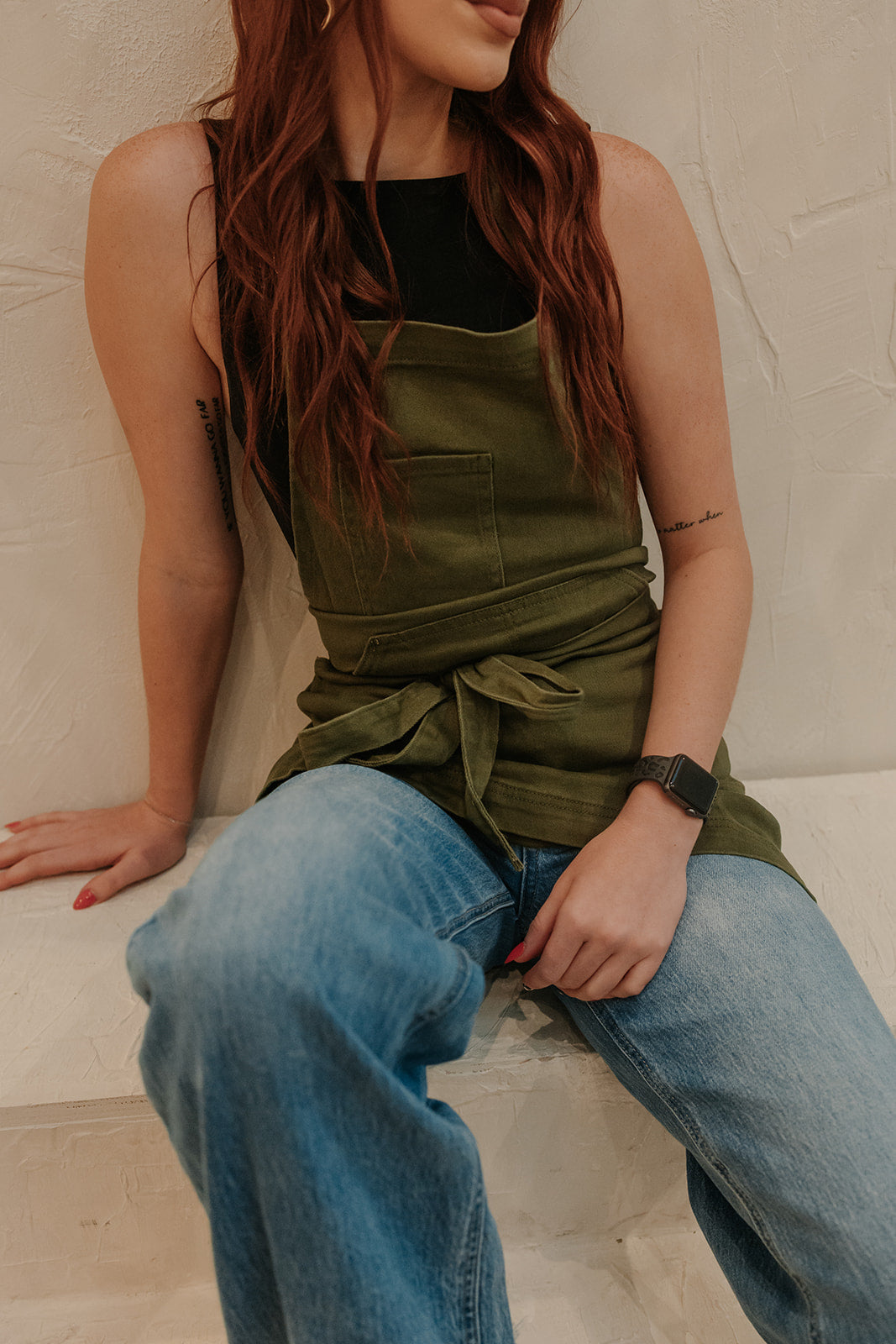 Petite female model sitting while wearing the Olive Green Apron by J Clark Designed.