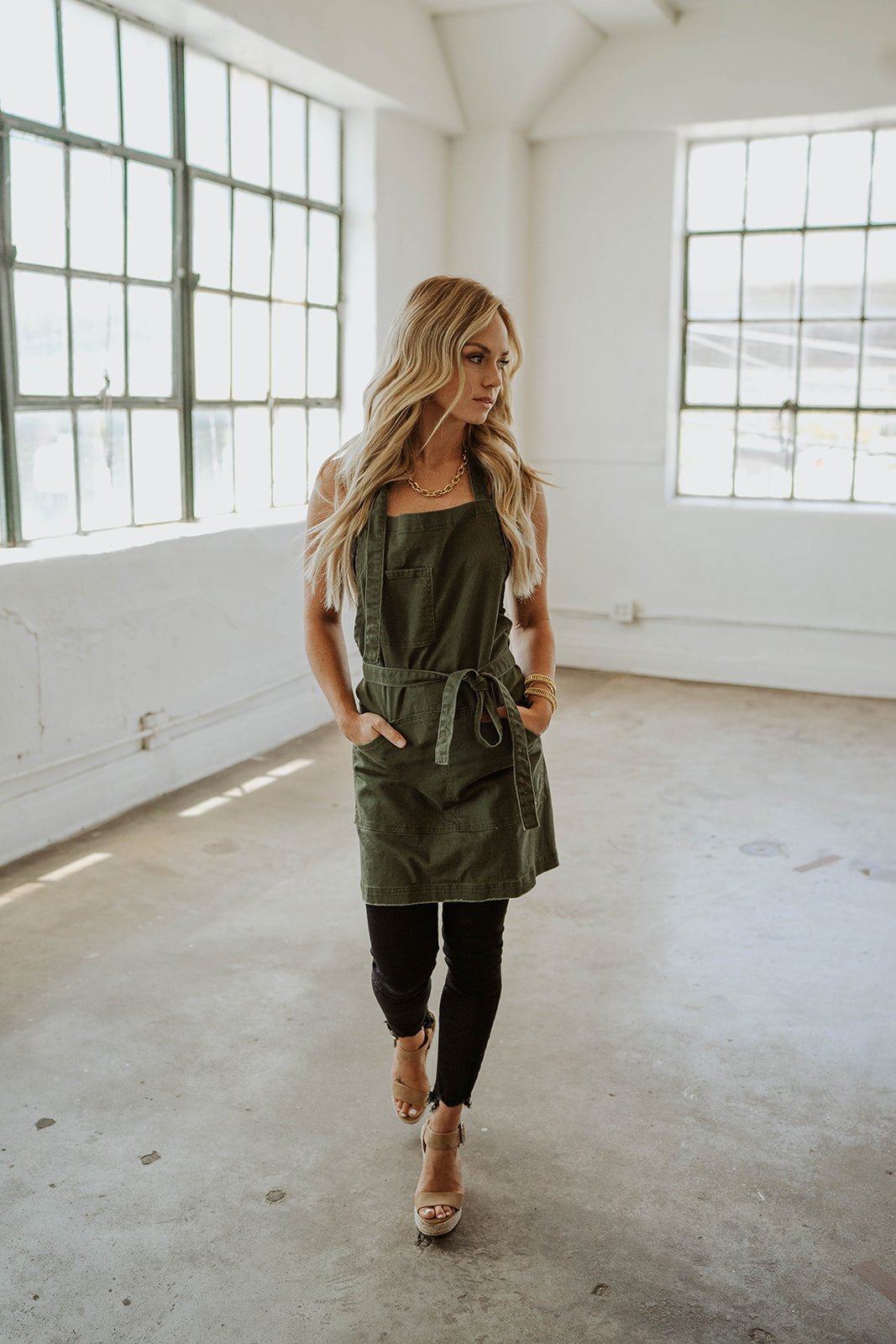 Female model walking while wearing Olive Green apron by J Clark Designed.