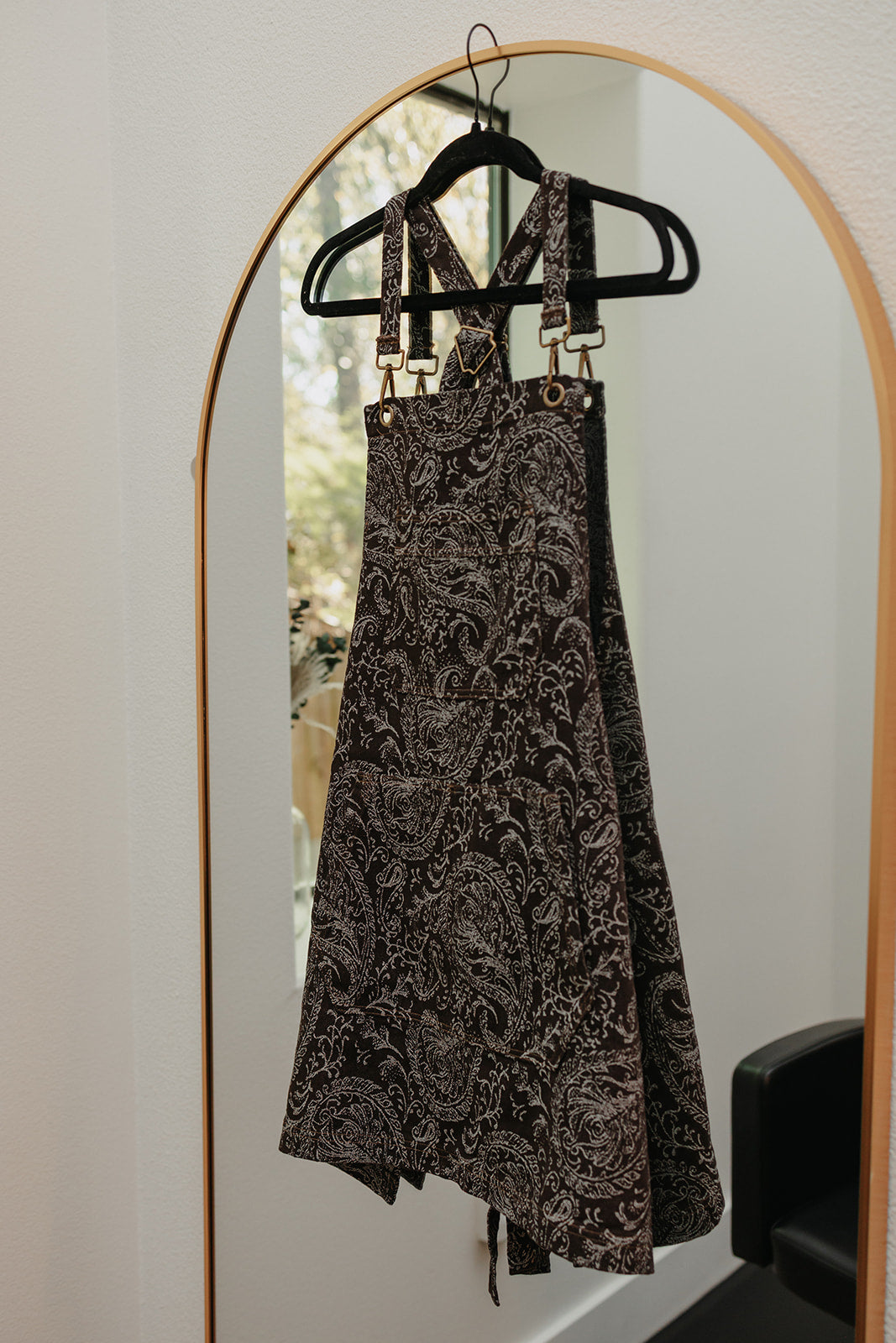 The Outlaw apron by J Clark Designed displayed on a hanger that is hung over a mirror